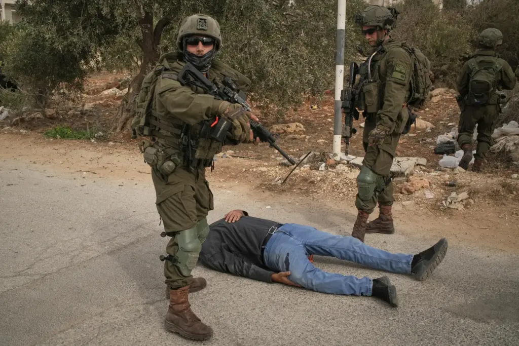 Israeli soldiers stand beside a wounded Palestinian man lying on...