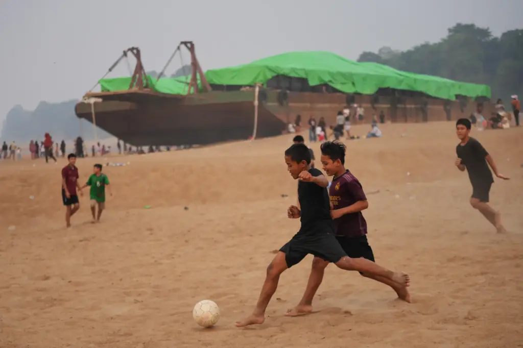 Kids play soccer near a barge stranded on a dry...