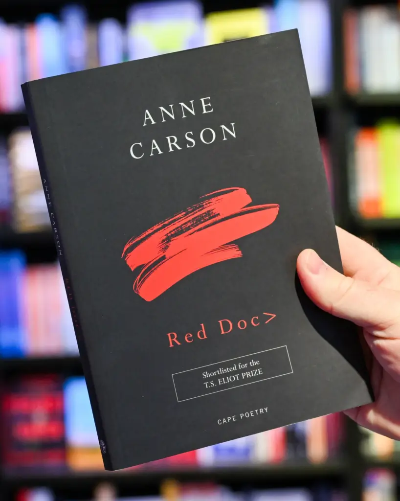 A man's hand holds Anne Carson's book 
