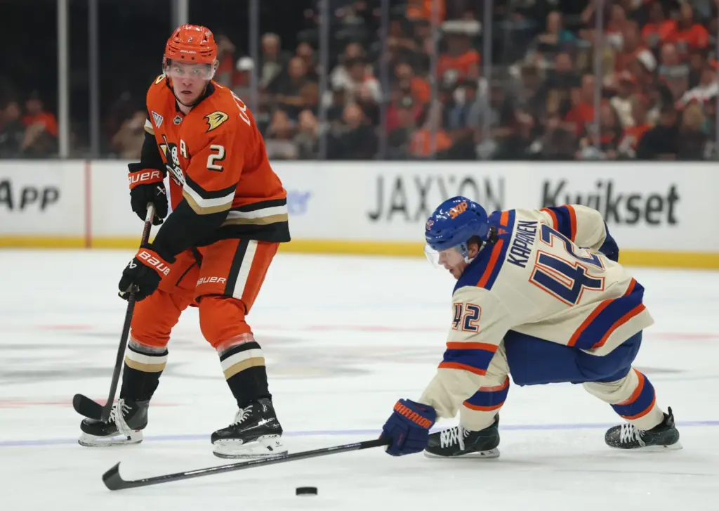 The Ducks’ Jackson LaCombe, left, passes the puck under the...