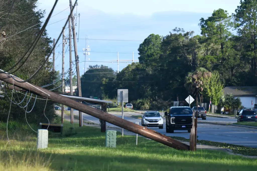 Vehicles pass a utility pole brought down by the effects...