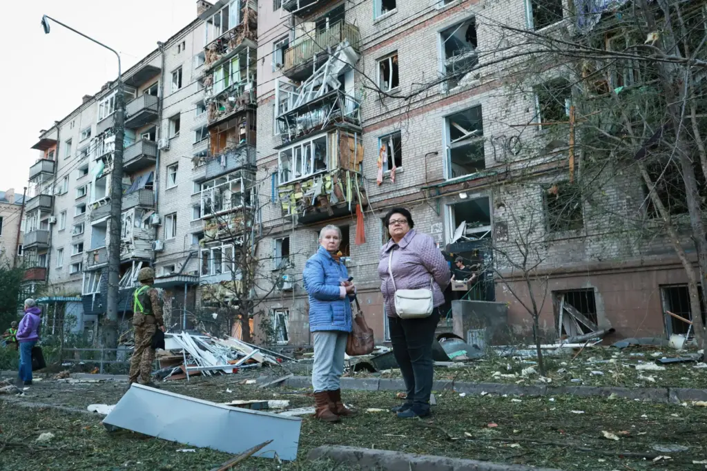 Local residents stand in front of building damaged by a Russian strike.