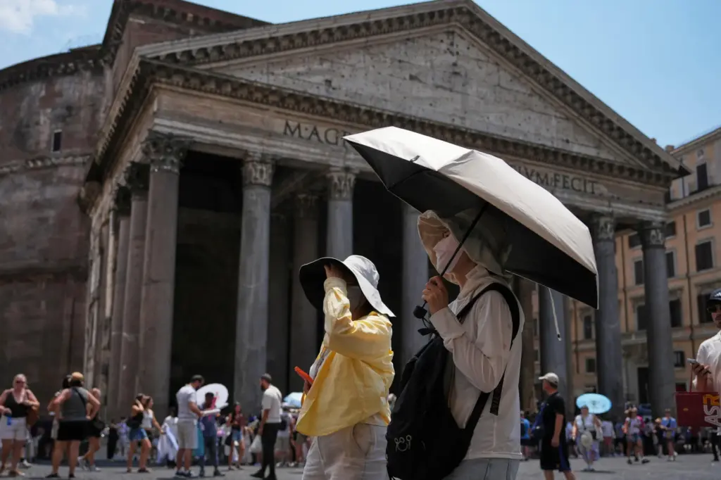 FILE – Tourists use umbrellas to take shelter from the...