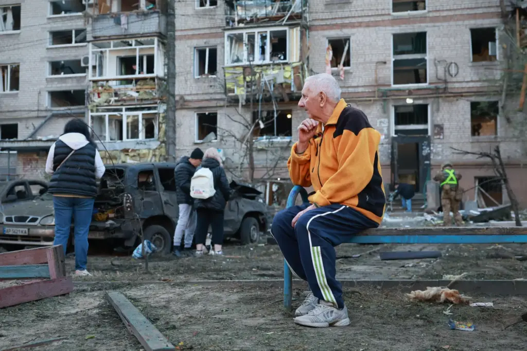 An elderly man sits on the bench in front of building damaged by a Russian strike.