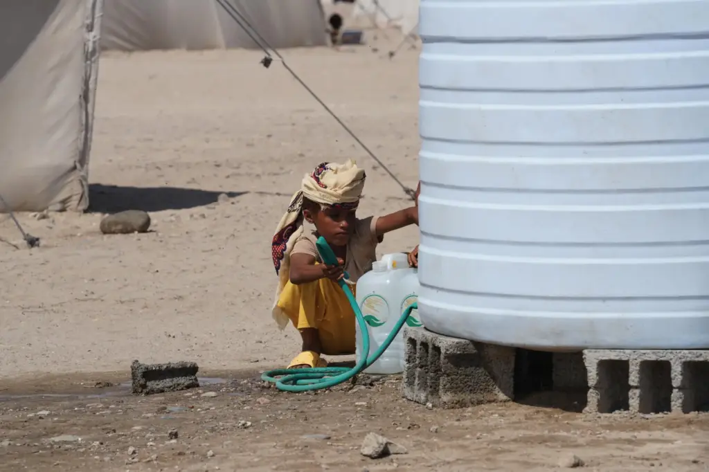 A displaced Yemeni boy fills water containers from a storage tank.