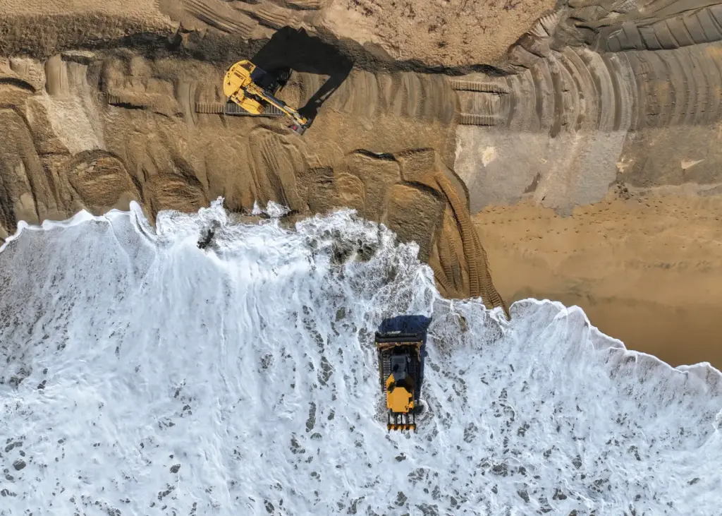 Workers build up a sand berm between homes and The...
