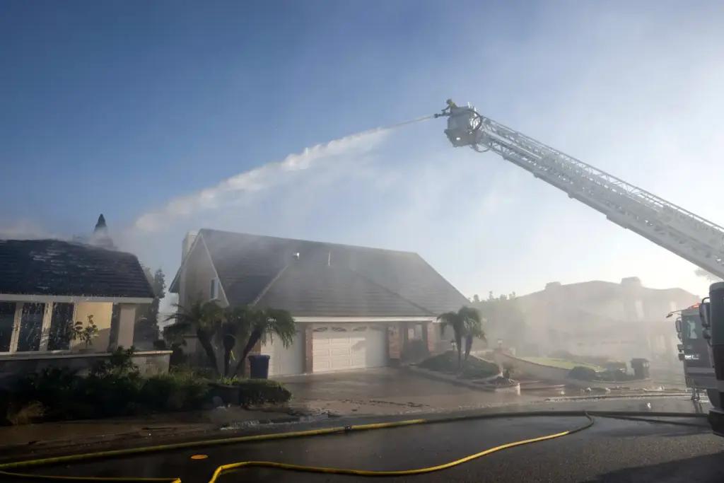 A firefighter on a ladder uses a hose to spray...