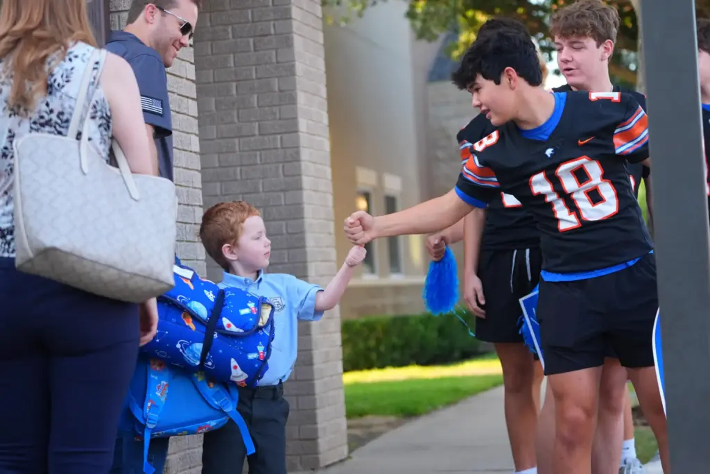 A high schooler greets an elementary school child on the first day of classes.