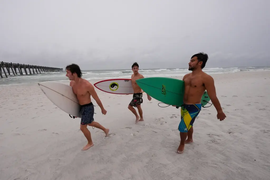 Surfers walk along the beach as Hurricane Isaias approaches Pensacola...