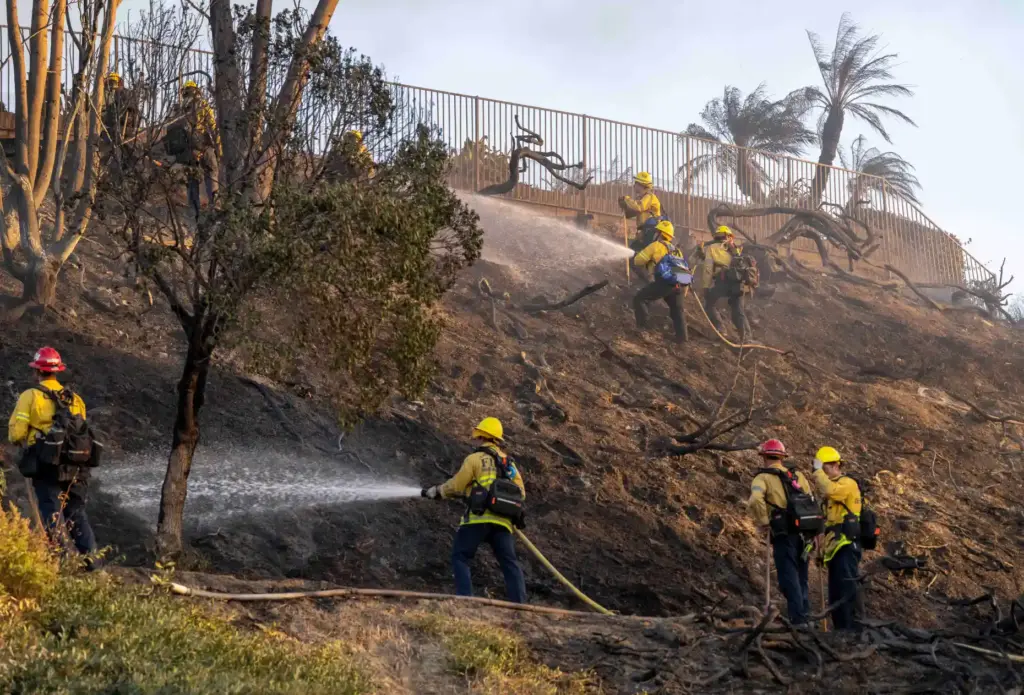 Firefighters work to extinguish flames on a hillside below a...
