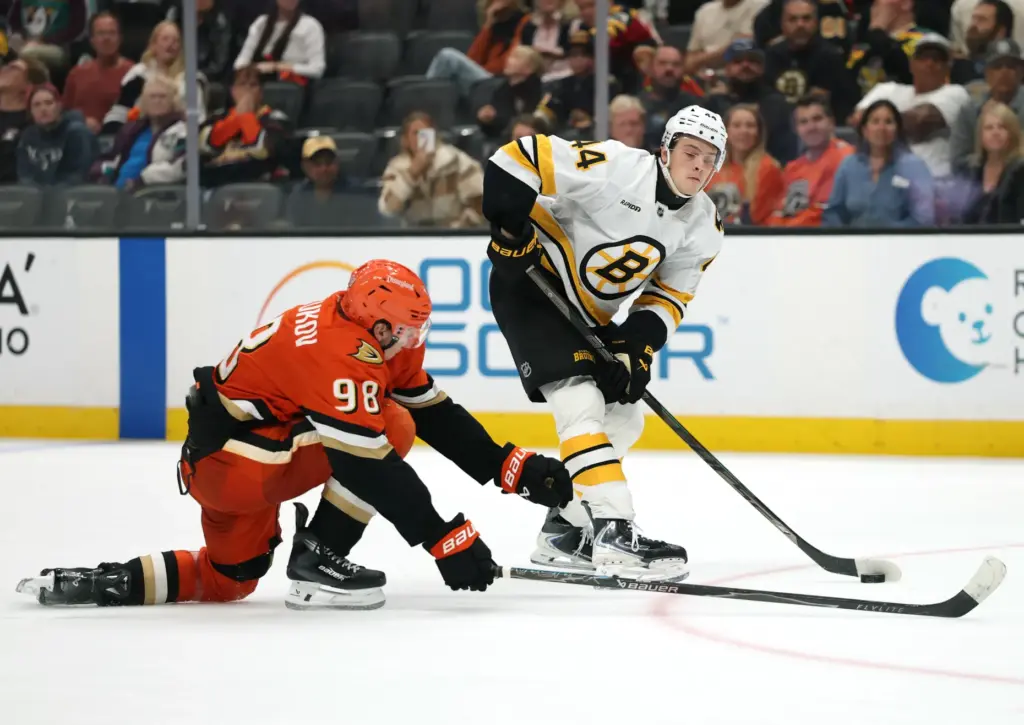 The Boston Bruins’ James Hagens, right, passes the puck as...