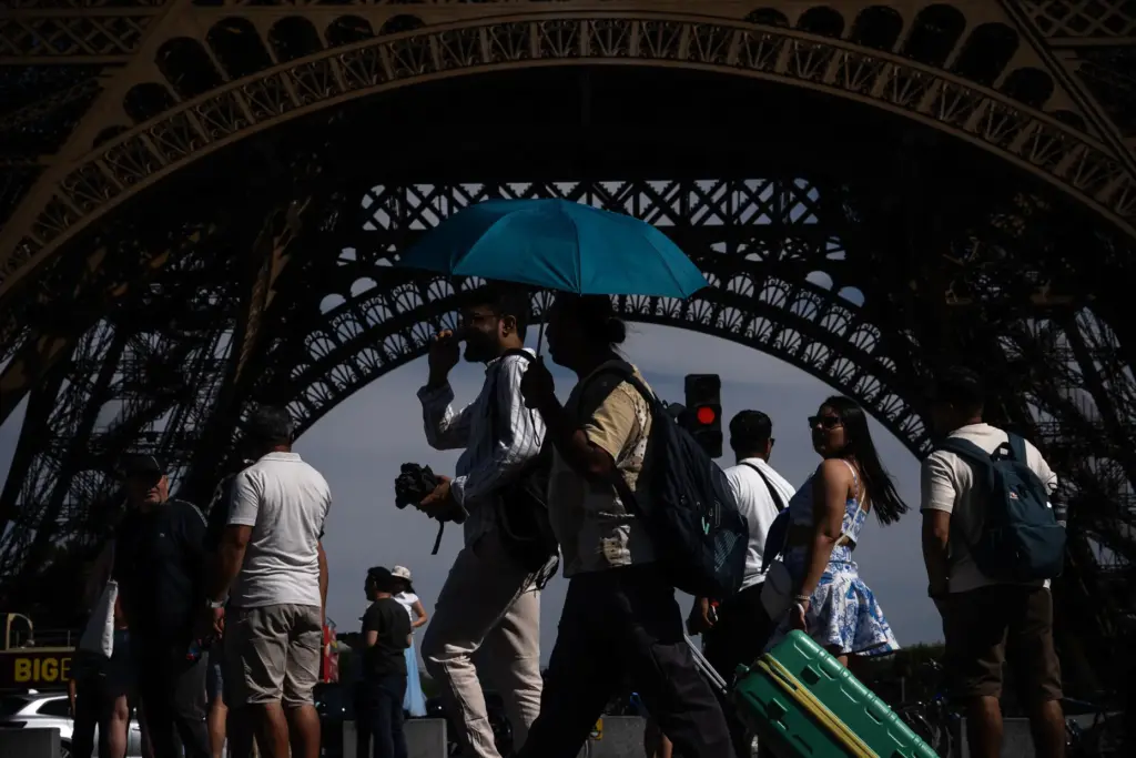 FILE – People walk with an umbrella near the Eiffel...