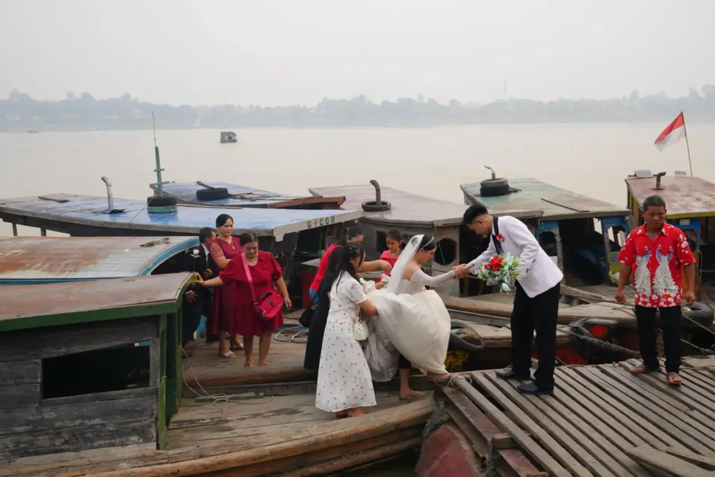 A groom helps a bride step between boats on the...