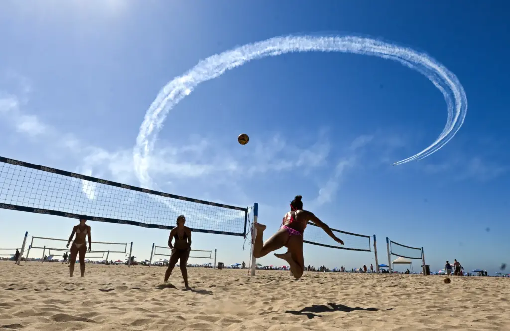 Beachgoers play volleyball as the Dawn Patrol Airshows Formation Team...