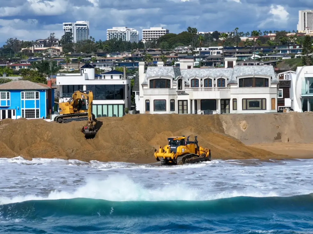 Workers build up a sand berm between homes and The...