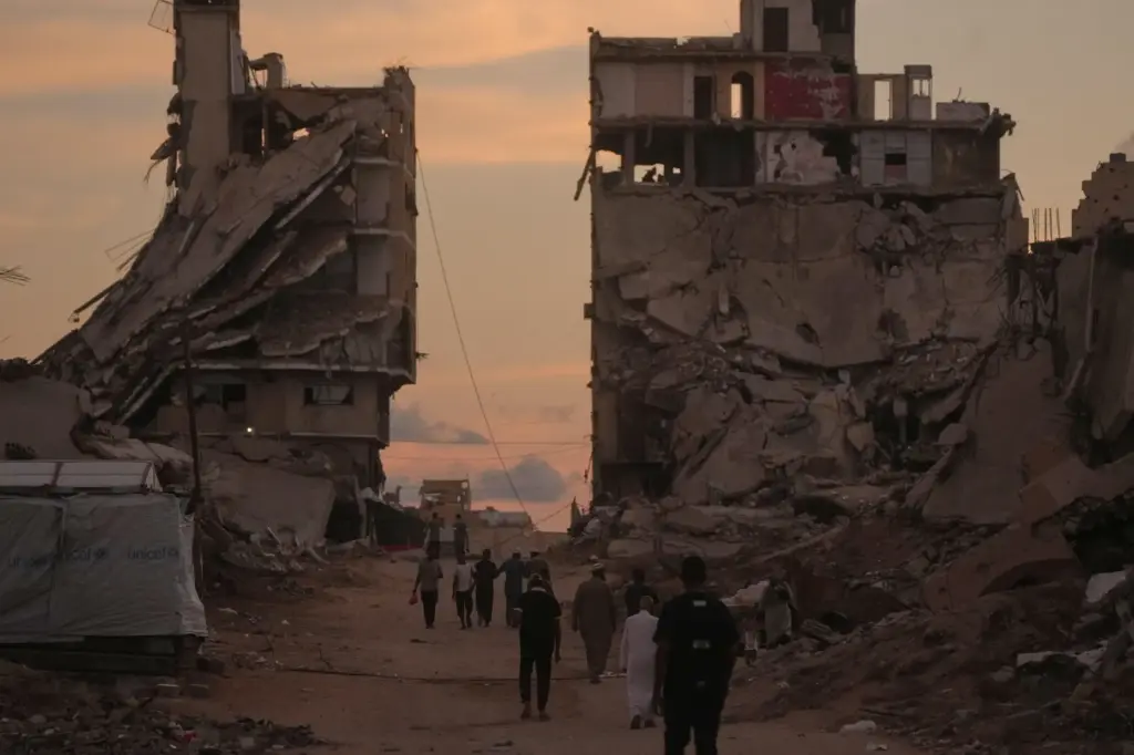 Palestinians walk along a street surrounded by buildings destroyed in Israeli military strikes.