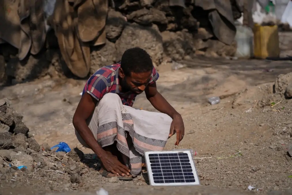 FILE – A displaced man inspects a small solar panel...