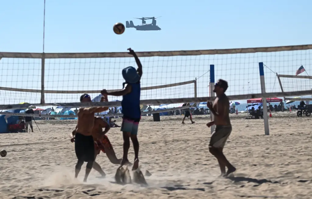 Beachgoers play volleyball as a United States Marine Corps MV-22...