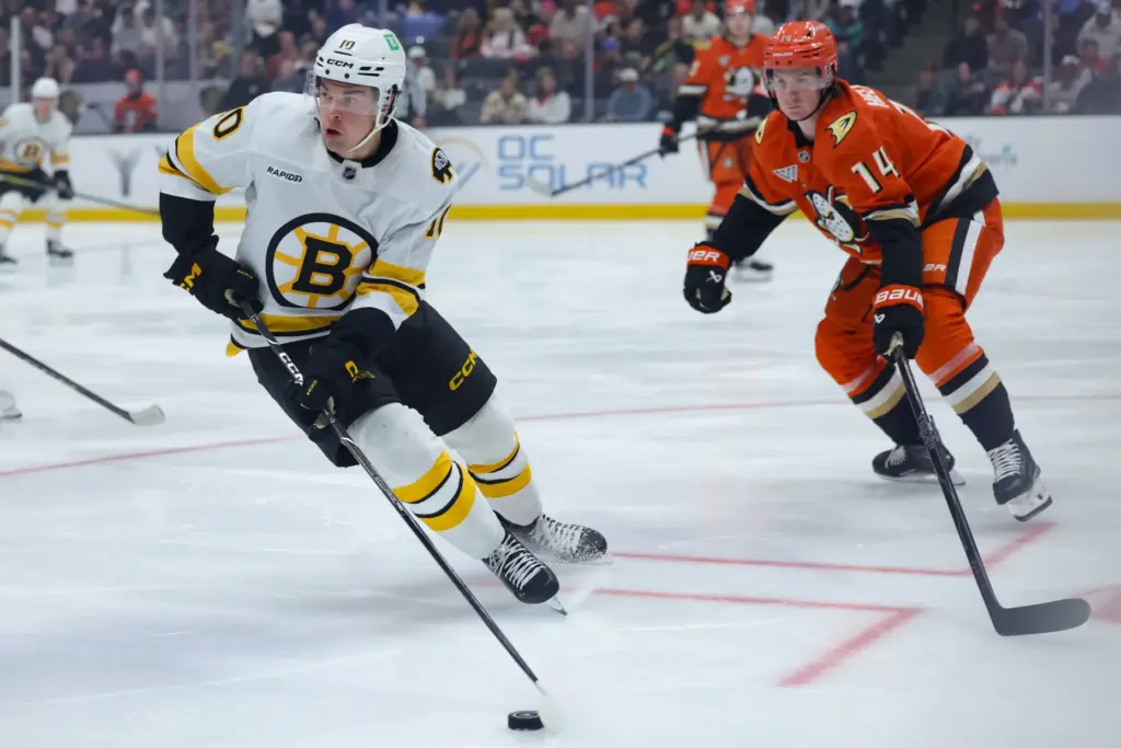 Boston Bruins right wing JJ Peterka, left, moves the puck...