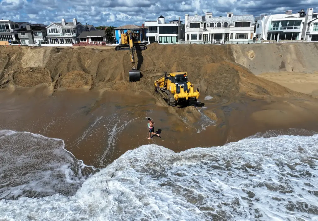 Workers build up a sand berm between homes and The...