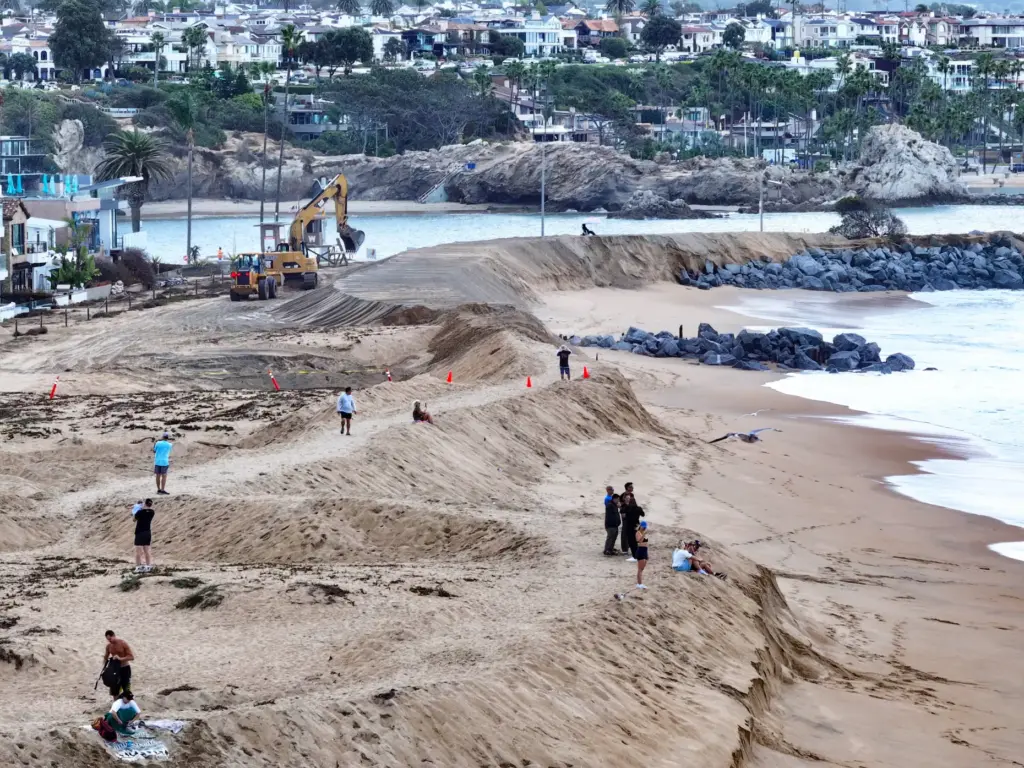 Workers build up a sand berm between homes and The...