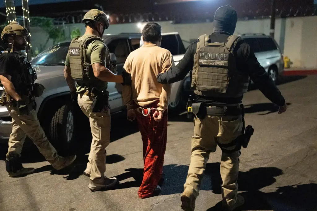 Homeland Security Investigations task force officers escort a suspect accused of illegally registering to vote.