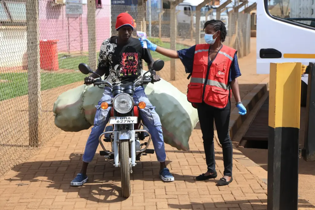 A Kenyan health worker checks the temperatures of travelers crossing from Uganda.