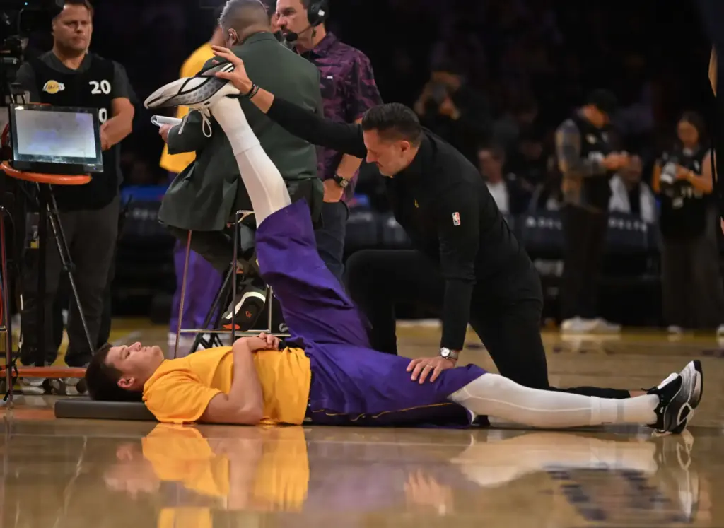Lakers center Walker Kessler, left, stretches with the help of...
