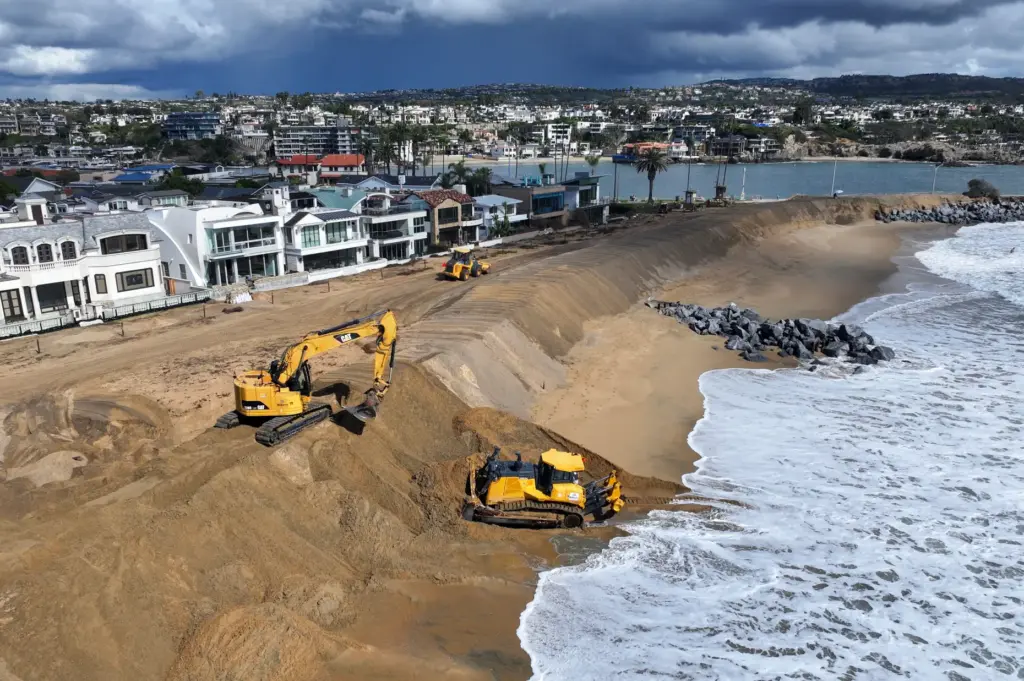 Workers build up a sand berm between homes and The...